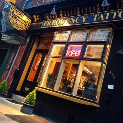 Frequency Tattoo Company storefront at night with warm golden light